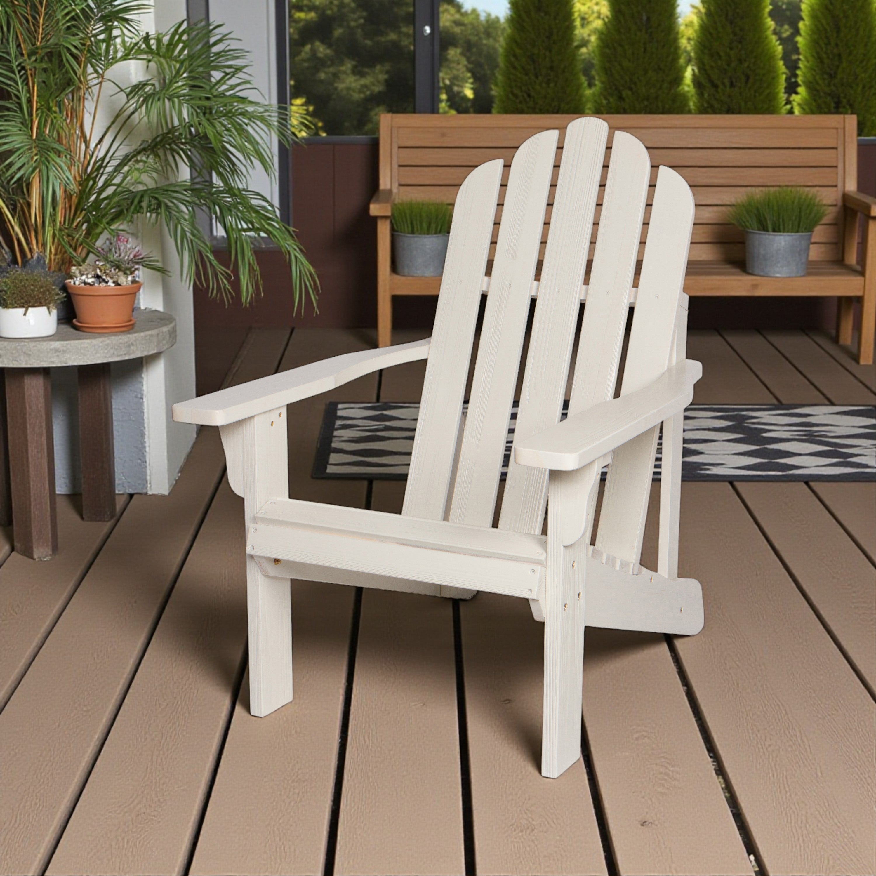 A white outdoor Adirondack chair placed on a brown deck, with potted plants, a bench, and greenery in the background. 