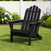 A black wooden Adirondack chair placed on a green lawn in front of a white fence with garden plants. 