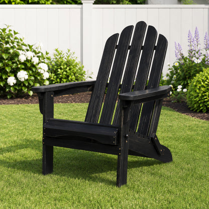 A black wooden Adirondack chair placed on a green lawn in front of a white fence with garden plants. 