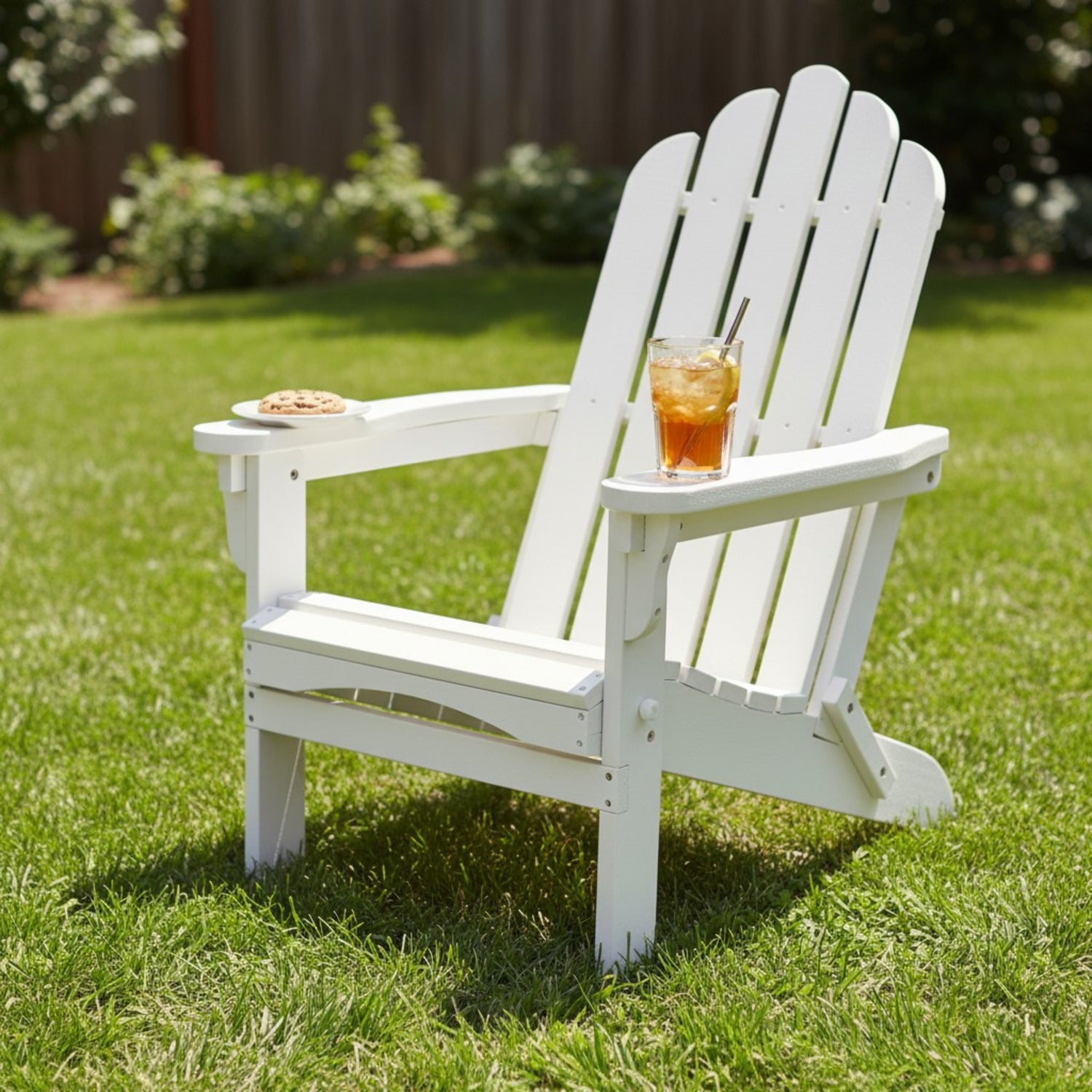 A white outdoor Adirondack-style chair on a green lawn, with a small plate and a glass of iced tea on its armrests. 