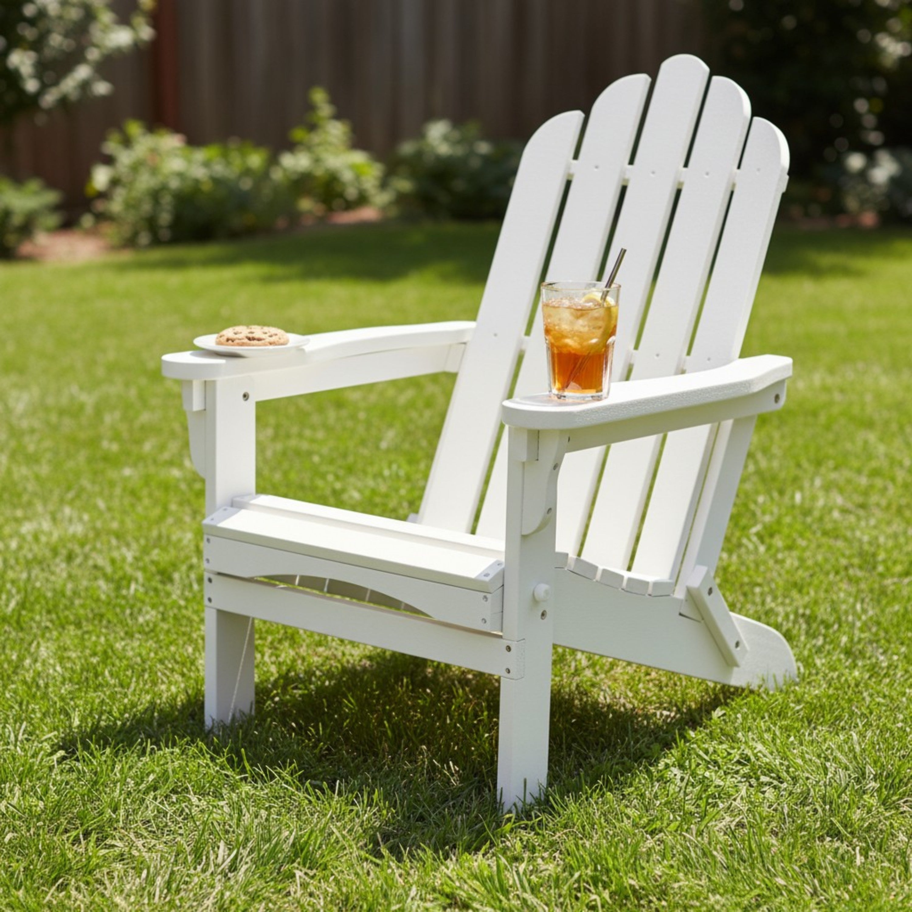 A white outdoor Adirondack-style chair on a green lawn, with a small plate and a glass of iced tea on its armrests. 