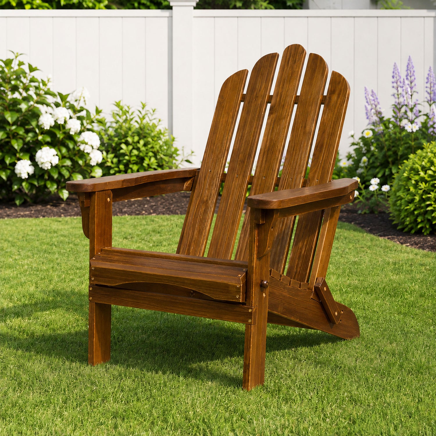 A brown wooden Adirondack-style outdoor chair on a green lawn with a white fence and garden plants in the background. 