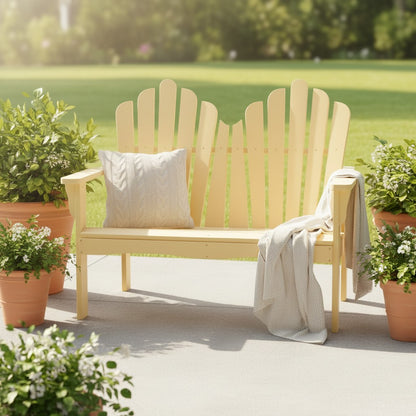 A light pastel yellow wood Adirondack-style outdoor bench with a slatted back, shown on a patio with potted plants and a throw blanket. A cream pillow rests on the bench.
