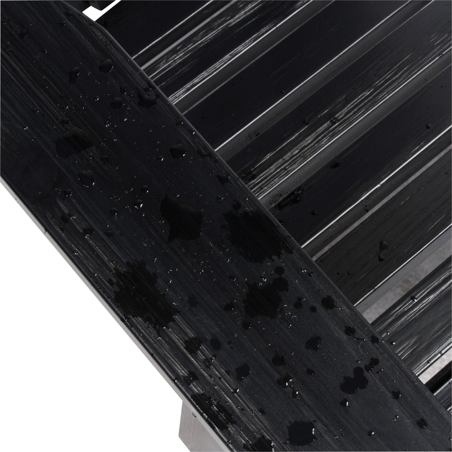 Close-up of a glossy black textured wooden slat surface showing the water resistant paint quality against a white background with diagonal black bars. 