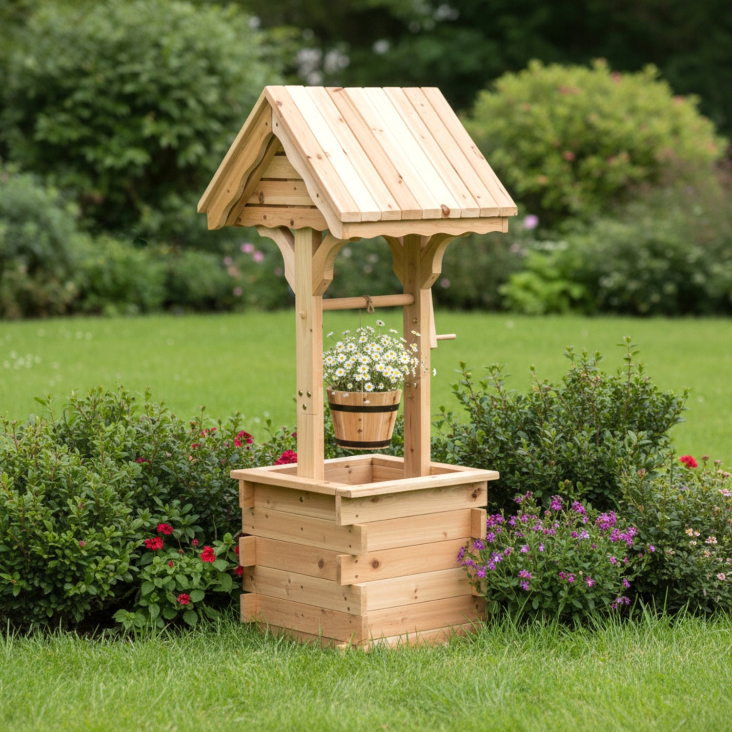 A small wooden garden well with a slatted bucket hanging from a curved roof, set on a grassy lawn surrounded by green shrubs and flowers. 