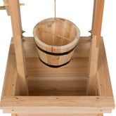 A wooden bucket with black metal bands hanging from a wooden frame on a white background. 