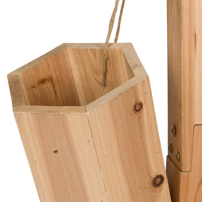 Close-up of a light natural wood hanging planter or container with a hexagonal cross-section, shown with a hanging twine loop and part of the adjacent wooden frame on a white background. 