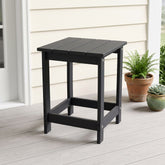A black outdoor side table with a slatted top and open frame legs, shown on a light porch next to potted plants. 