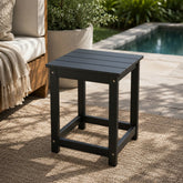 Black outdoor side table on a patio with a pool in the background 
