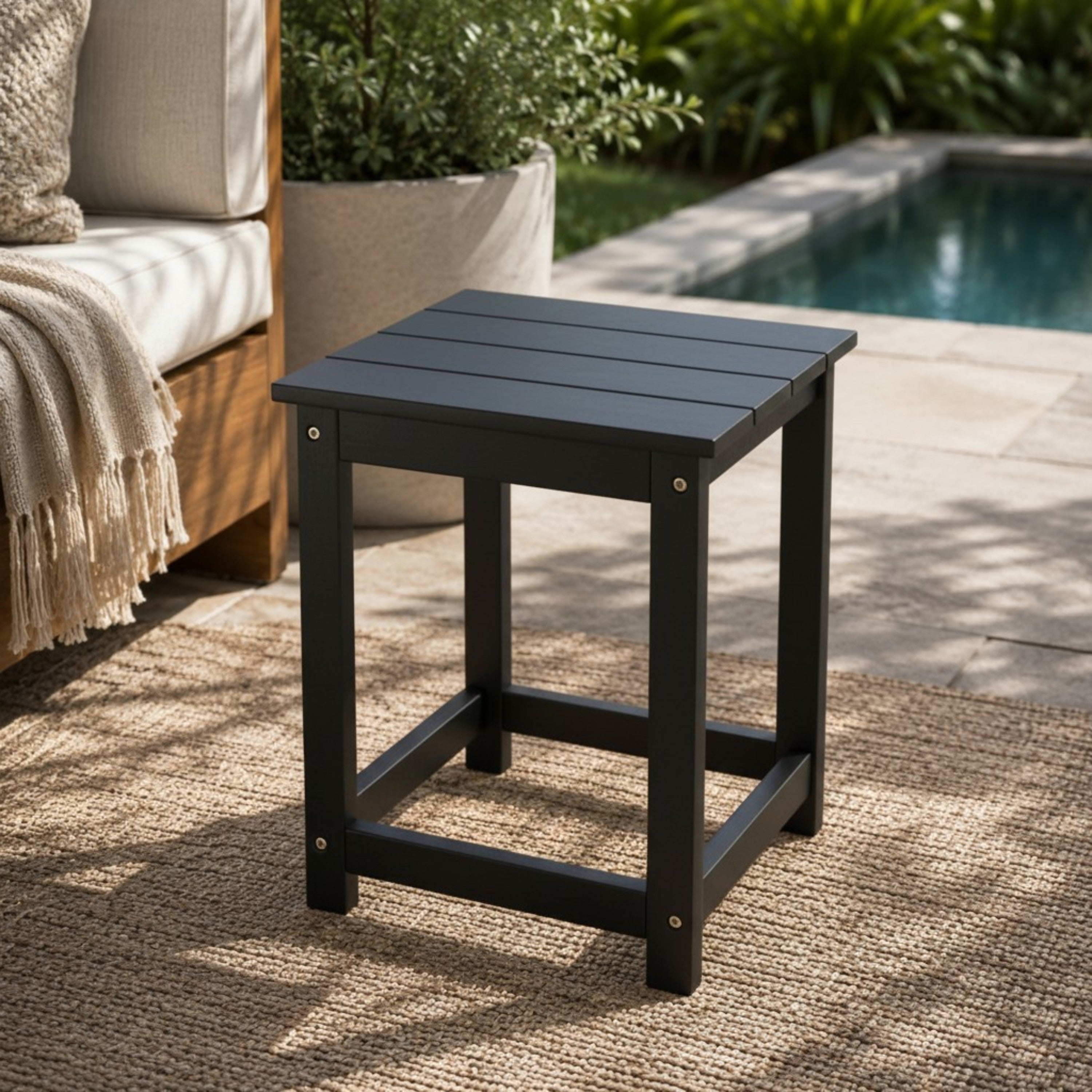 Black outdoor side table on a patio with a pool in the background 