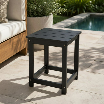 Black outdoor side table on a patio with a pool and garden in the background 