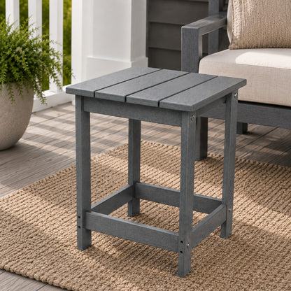 A gray outdoor side table with a slatted top and open lower support frame, shown on a woven rug beside a patio chair in a porch setting. 
