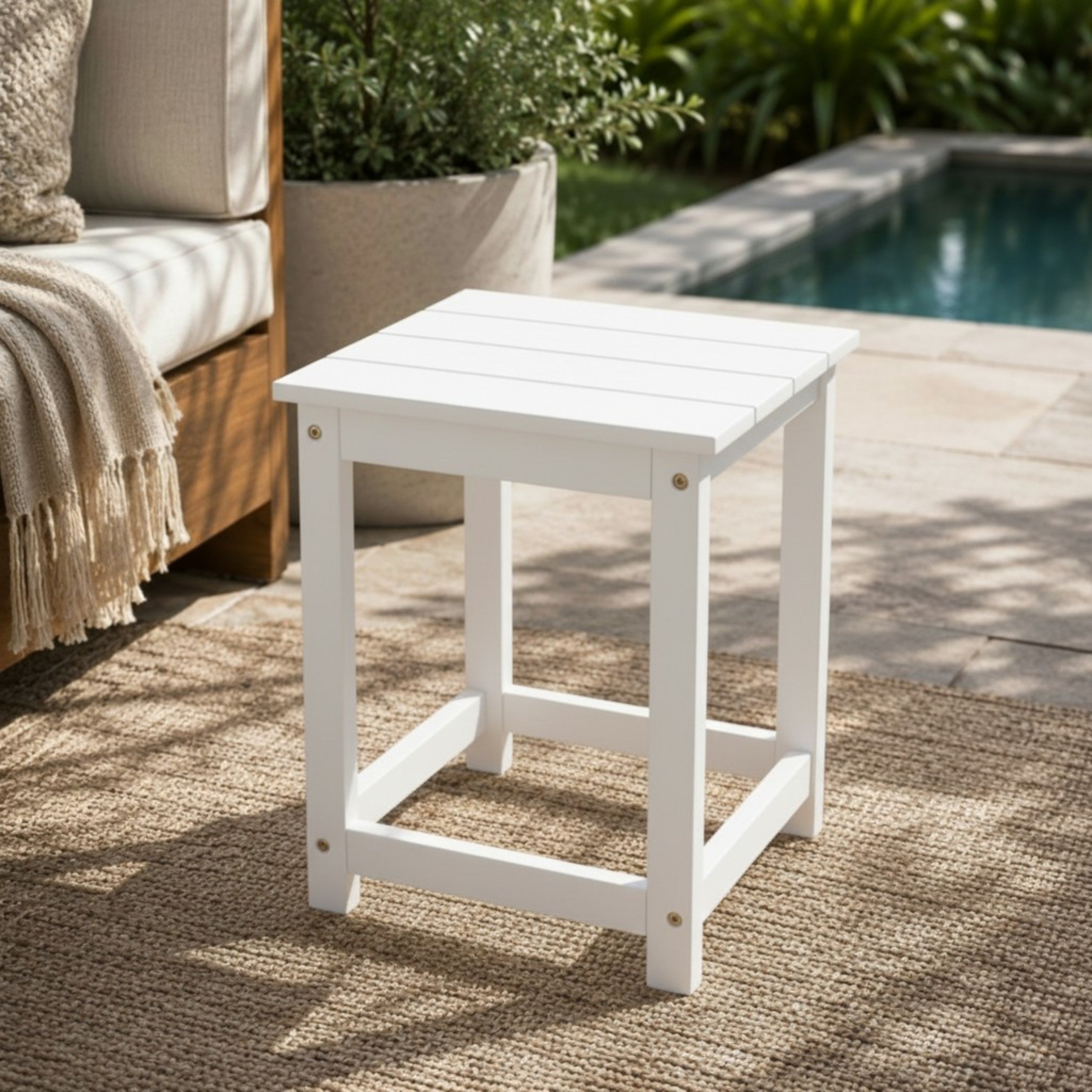 White outdoor side table on a patio with a pool in the background 