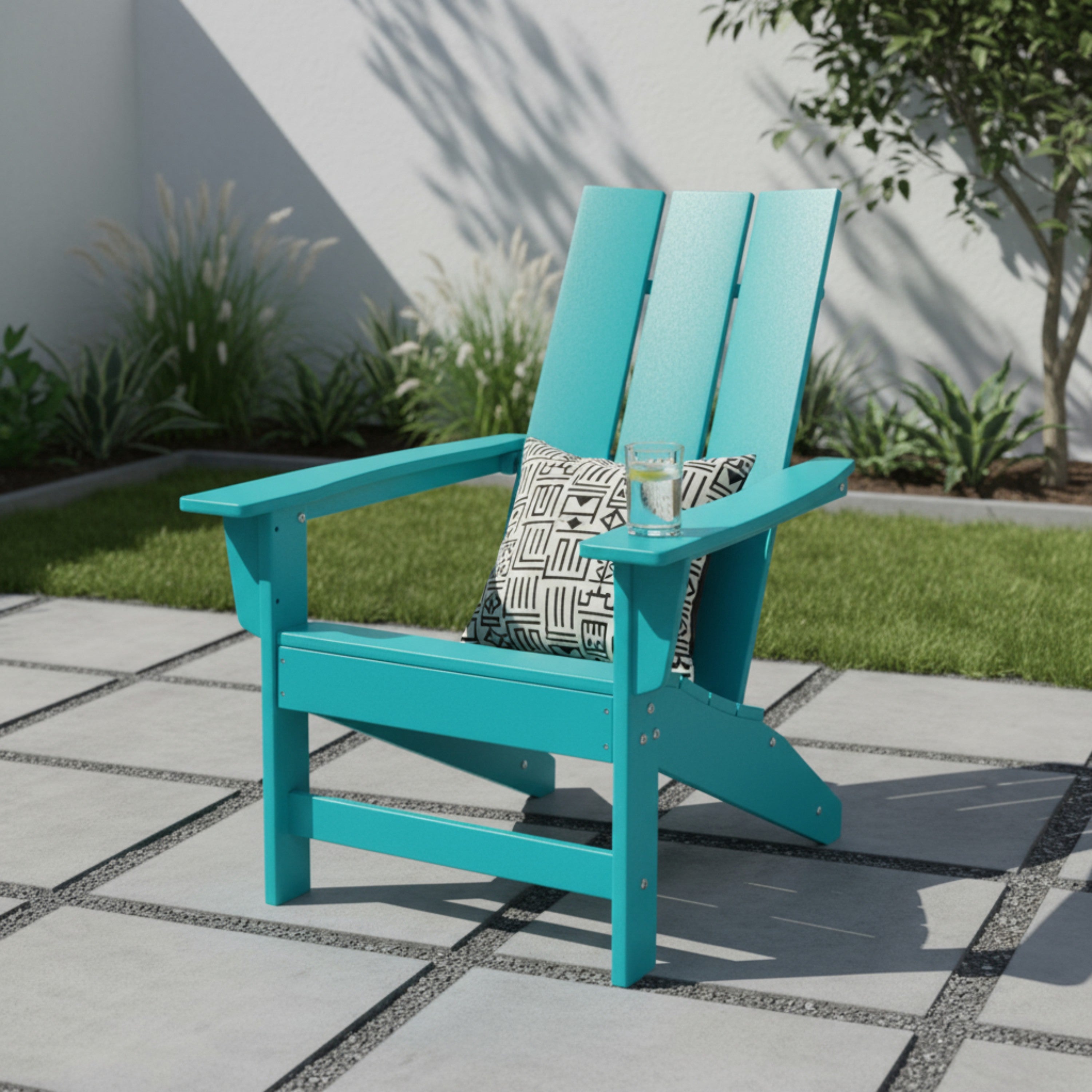 A turquoise Adirondack-style outdoor chair on a paved patio with a black-and-white patterned throw pillow and a glass of water, set against a white wall and green plants. 