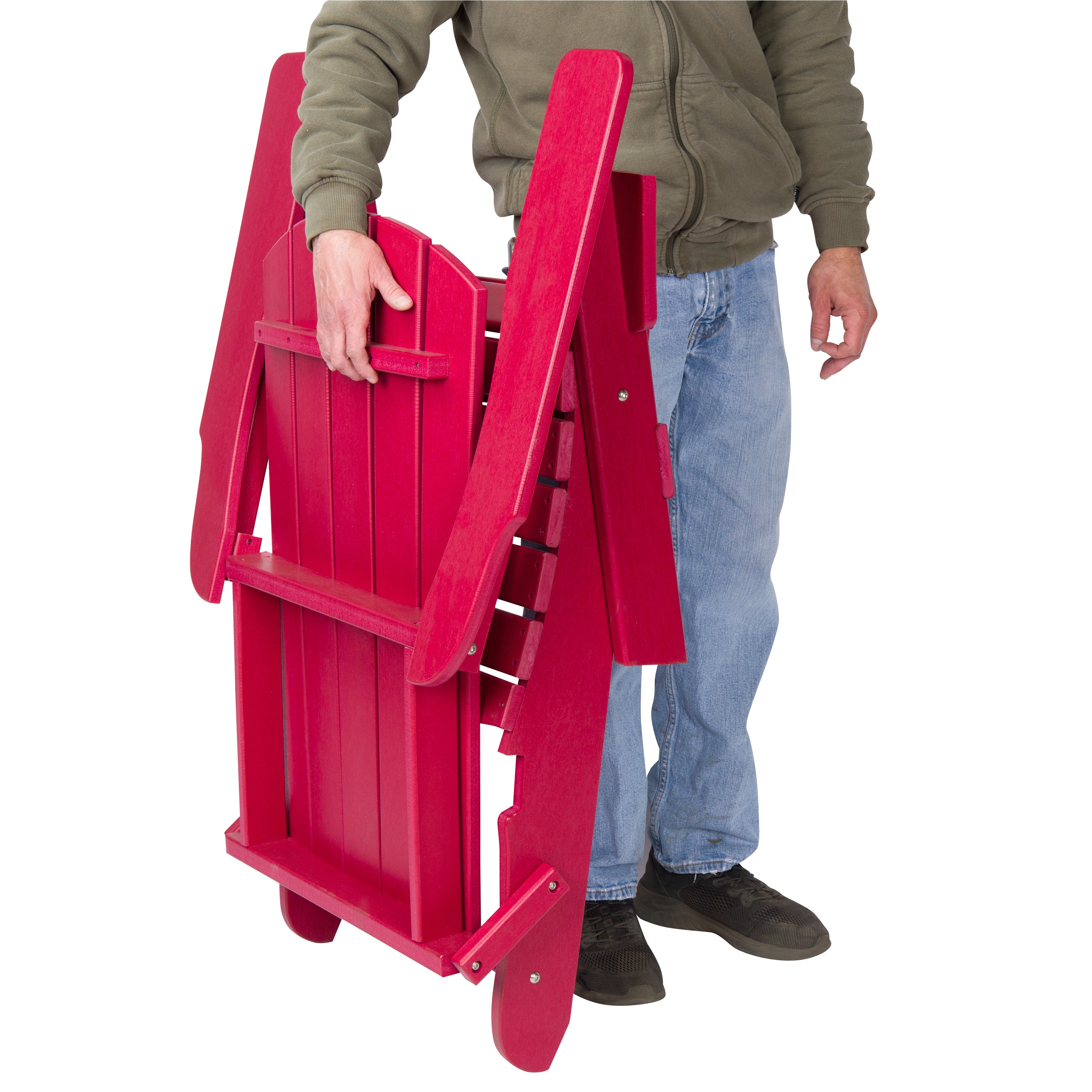 A person in a green zip-up jacket, blue jeans, and black shoes is holding a folded bright red wooden folding chair against a plain white background. 