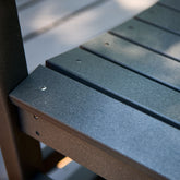 Close-up of black slatted outdoor furniture seating with a matching dark frame, showing the textured plastic or composite material and screw fasteners. 