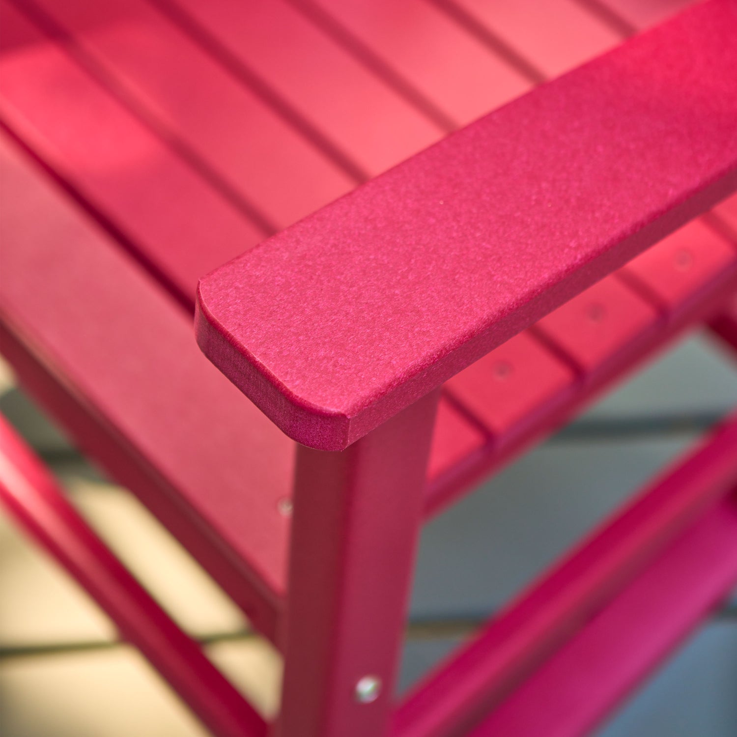 Close-up of a red slatted outdoor chair showing the armrest corner and frame construction. 