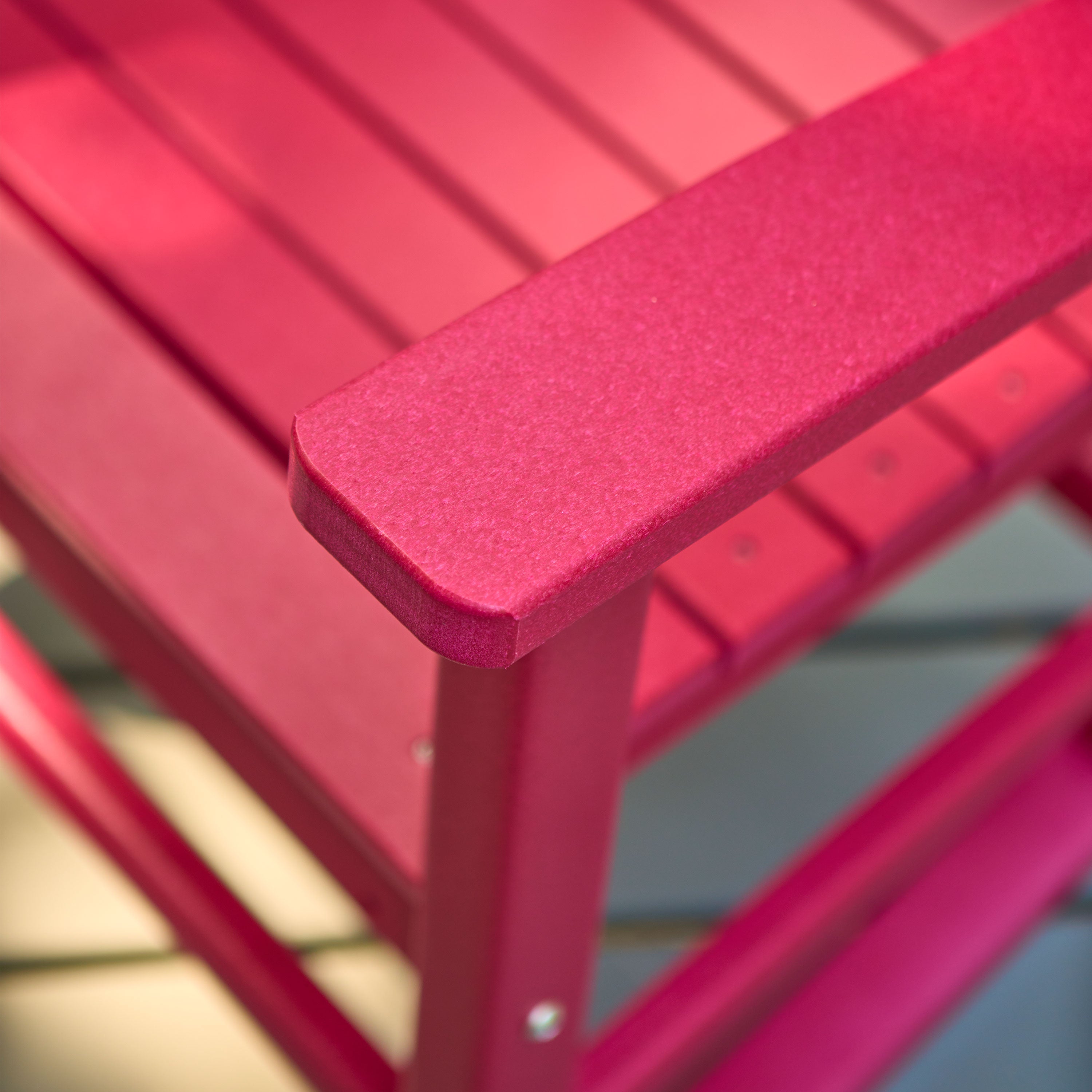 Close-up of a red slatted outdoor chair showing the armrest corner and frame construction. 