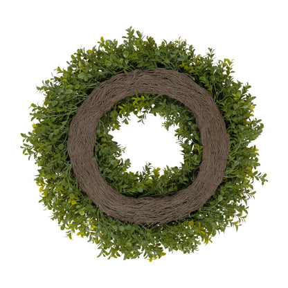 An artificial greenery wreath with dense green boxwood-style foliage and a rustic brown woven vine center, shown on a plain white background.